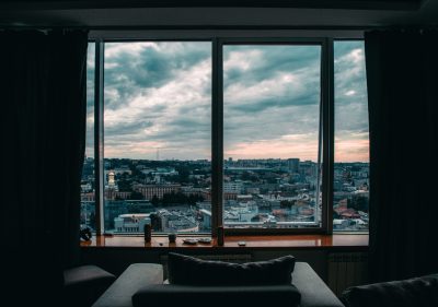 This is a large window framed by curtains. There is a chair in front of the window. Sitting in it, you can enjoy a beautiful view of the city.